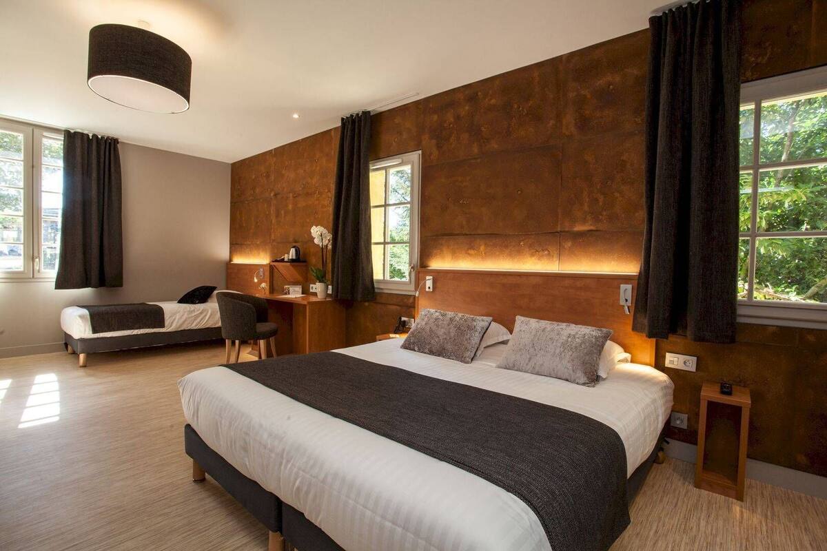 Un dormitorio moderno con una cama grande, un escritorio y una silla. Hay dos ventanas con cortinas, y la habitación tiene una pared de madera decorativa.