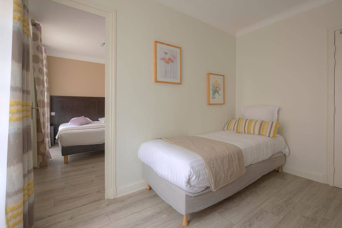 Un dormitorio con cama, mesita de noche y espejo. Hay dos cuadros enmarcados en la pared.