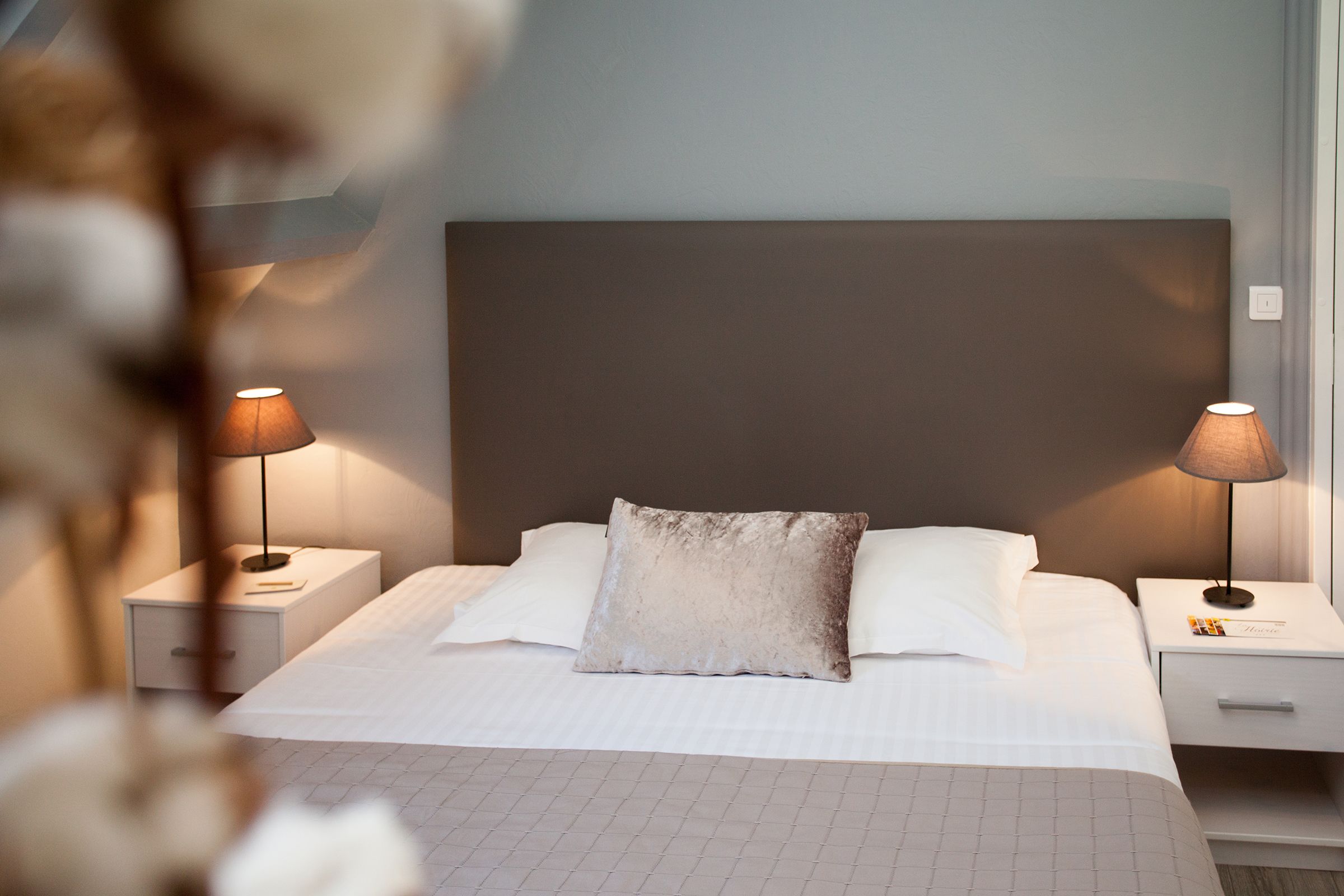 A neatly made bed with white linens, two bedside lamps, and a large headboard.