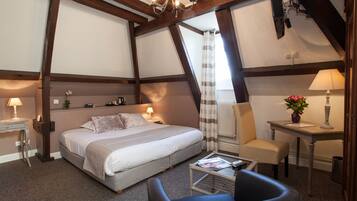 Een slaapkamer met een groot bed, een bureau, een stoel en een klein tafeltje met een lamp.