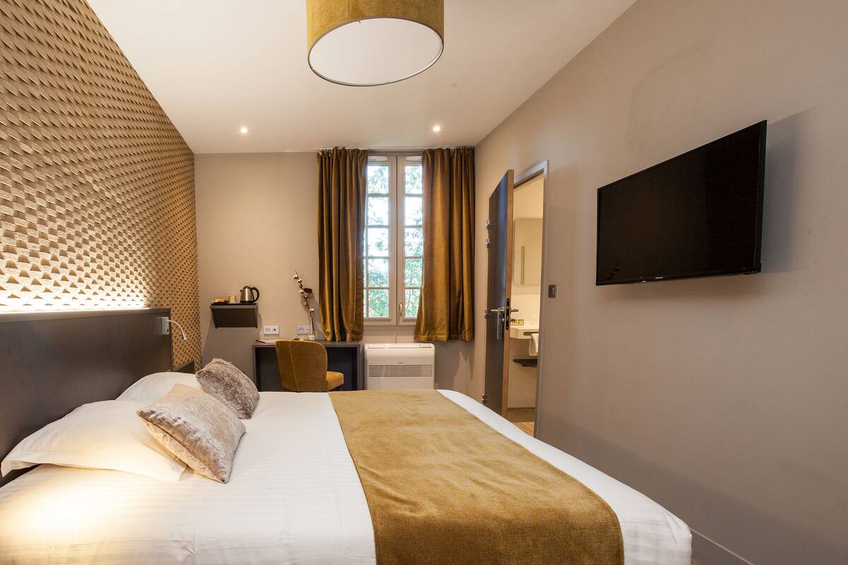 Habitación de hotel con una cama grande, un televisor de pantalla plana en la pared, un escritorio con silla y una ventana con cortinas.