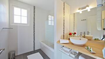 Un baño con bañera, lavamanos con espejo y ventana.