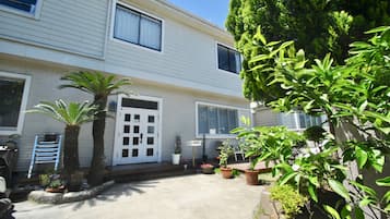 A two-story house with a front porch, potted plants, and a palm tree.