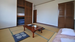 Una habitación japonesa tradicional con suelo de tatami, una mesa de madera baja, una cama con colcha rosa y puertas correderas de madera.
