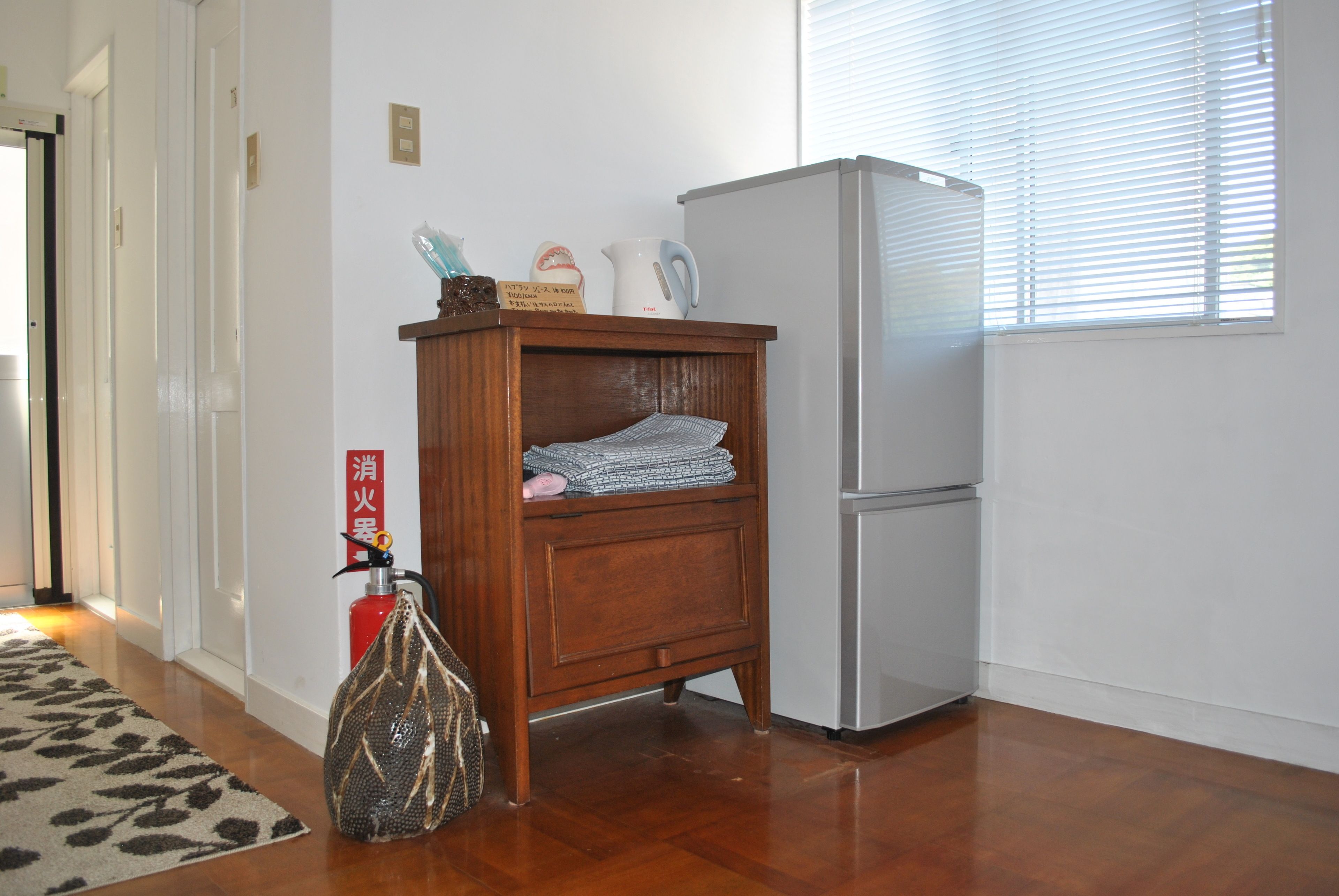 A room with a wooden cabinet, a white refrigerator, a fire extinguisher, and a patterned rug.