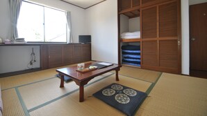Una habitación japonesa tradicional con suelo de tatami, una mesa de madera baja, un futón como cama, un armario de madera corredera y una ventana con cortinas.