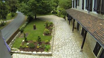 A stone-paved courtyard with a grassy area, a pathway leading to a building with a tiled roof and dark shutters.