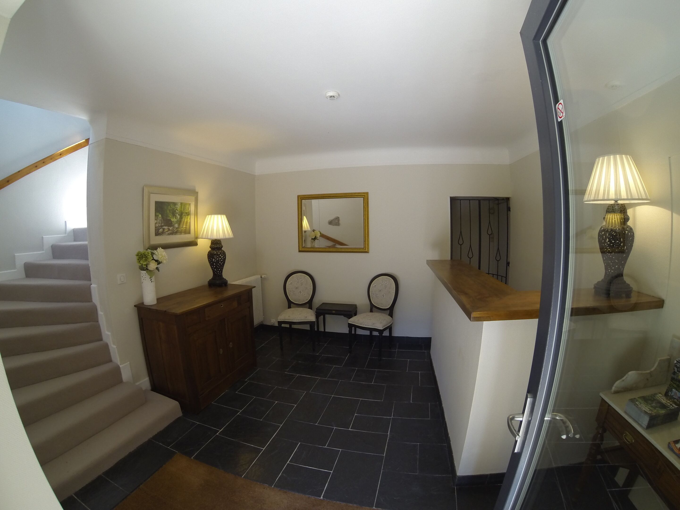 A hallway with a staircase, a wooden desk with a lamp, two chairs, a framed picture, and a radiator.