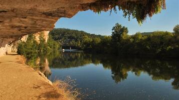 A serene river scene with a bridge, a sandy path, and lush greenery.