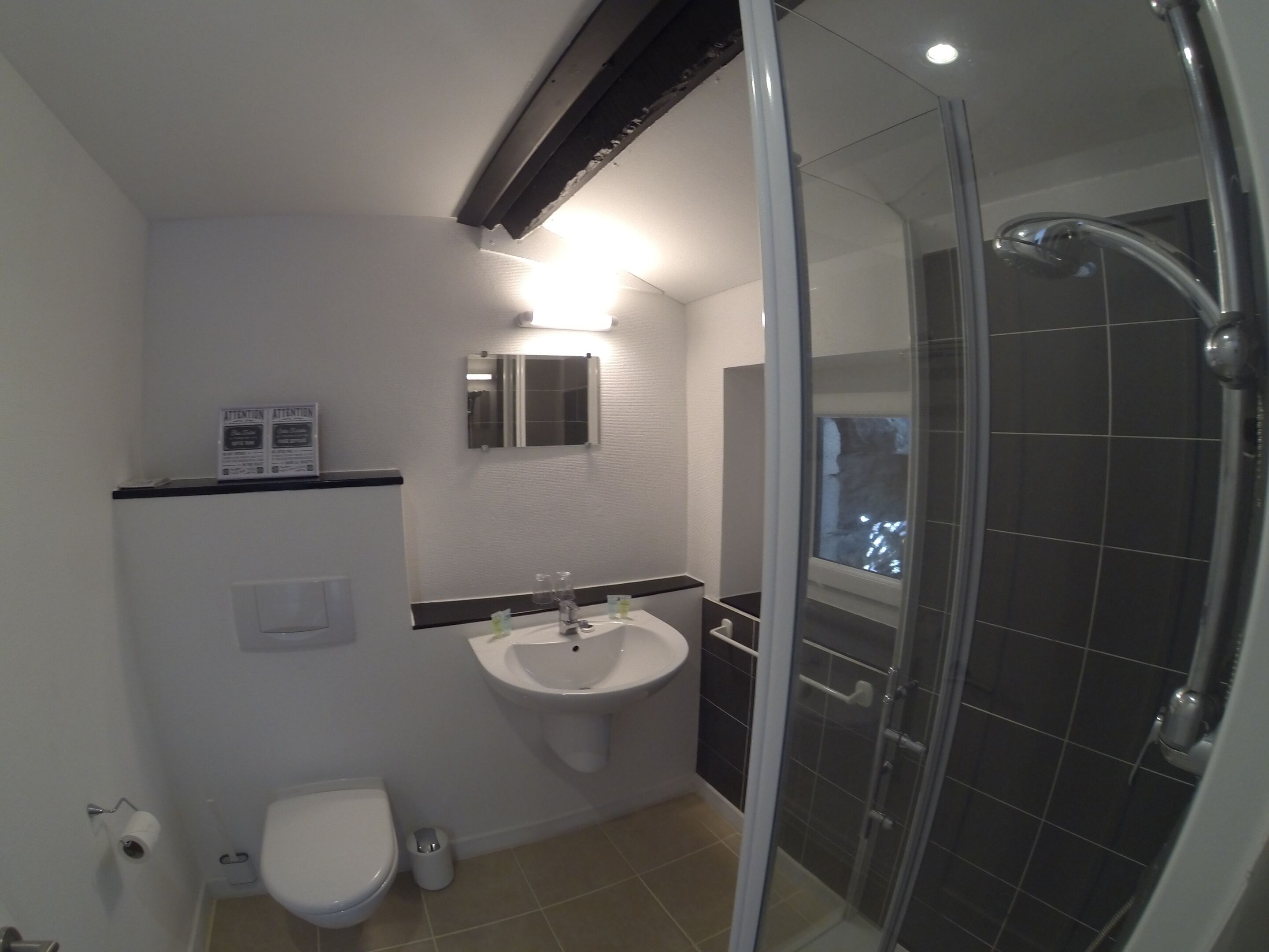 A bathroom with a toilet, sink, mirror, and a glass-enclosed shower.