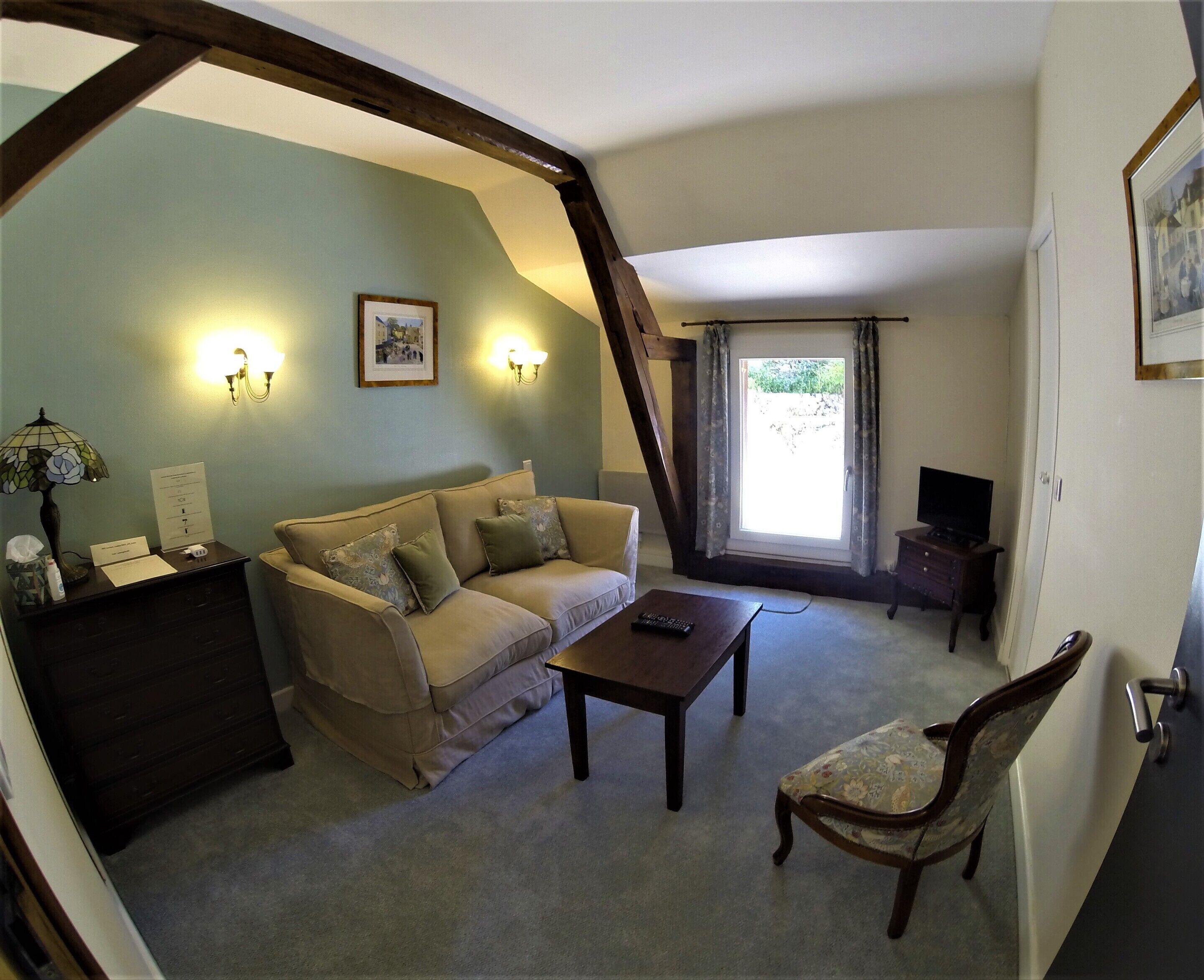 Una sala de estar con un sofá, una mesa de centro, una silla, un mueble para televisión y una ventana con cortinas.