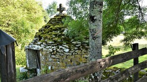 A rustic stone structure with a cross on top, surrounded by greenery and a wooden fence. - Auberge de la Sagne (Cabrerets)