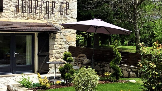 A stone building with a patio area featuring a table, chairs, and a large umbrella. - Auberge de la Sagne (Cabrerets)