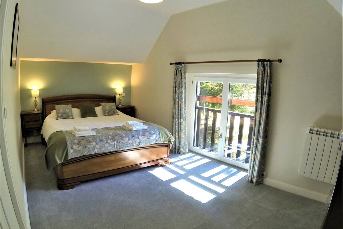 A bedroom with a bed, bedside lamps, a radiator, and a view through a window.