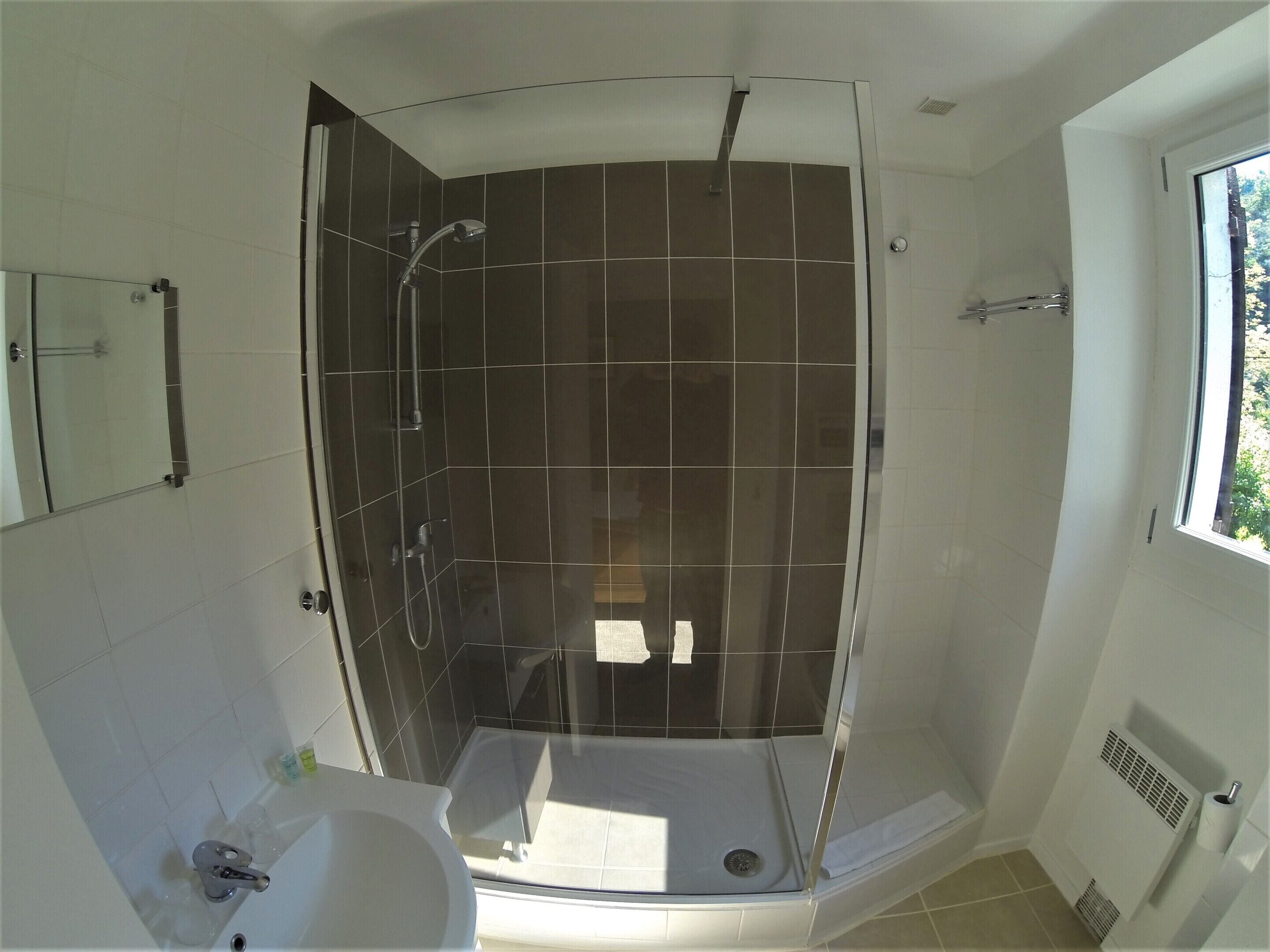 Una doccia con porta in vetro, un lavandino e una finestra.