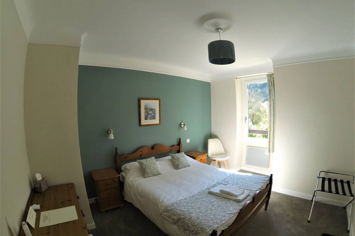 A bedroom with a bed, bedside tables, a chair, a window, and a ceiling light.