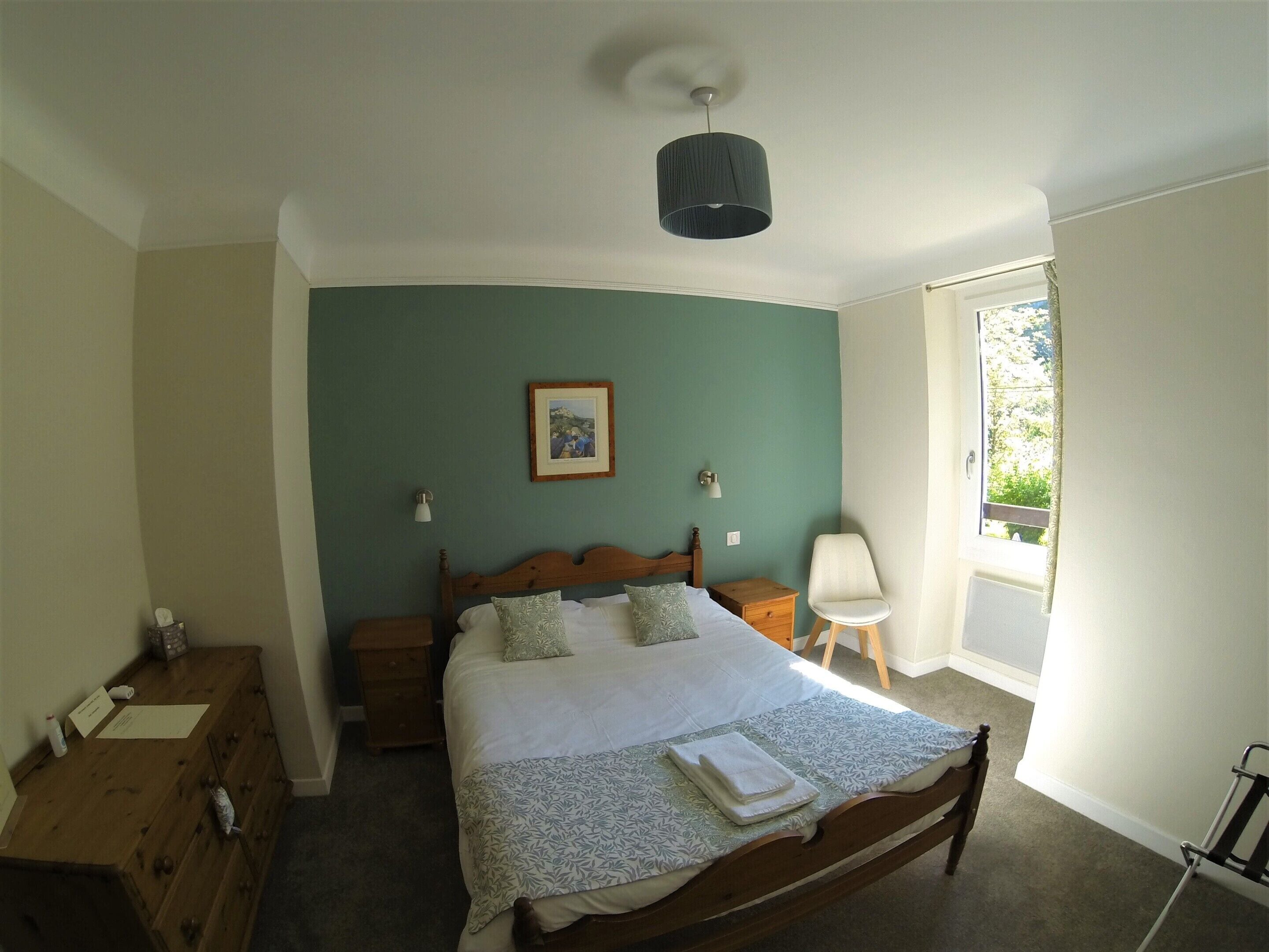 A bedroom with a bed, bedside tables, a chair, a window, and a ceiling light.
