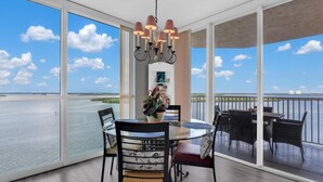 A dining area with a glass table and chairs, a chandelier, and a view of the sea through large windows. - Spectacular Views!!  Beautifully Updated!!  No Resort Fees! (Fort Myers Beach)