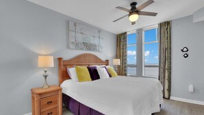 A bedroom with a bed, nightstands, a ceiling fan, a window with curtains, and a wall-mounted artwork. - Spectacular Views!!  Beautifully Updated!!  No Resort Fees! (Fort Myers Beach)