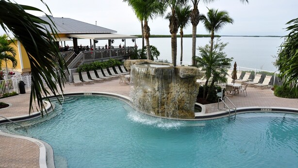 A pool with a waterfall feature, surrounded by lounge chairs and palm trees. - Spectacular Views!!  Beautifully Updated!!  No Resort Fees! (Fort Myers Beach)