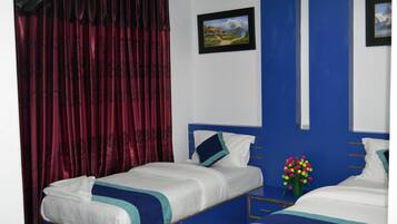 Una habitación con dos camas, cortinas rojas, un cuadro en la pared y un florero con flores.