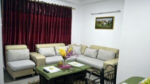 A living room with a beige sofa, a coffee table with a vase of flowers, and a red curtain. - Nana Homes (Kathmandu)