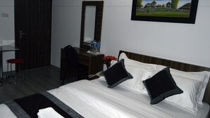 A hotel room with a bed, a desk, a chair, a mirror, and a painting on the wall. - Nana Homes (Kathmandu)