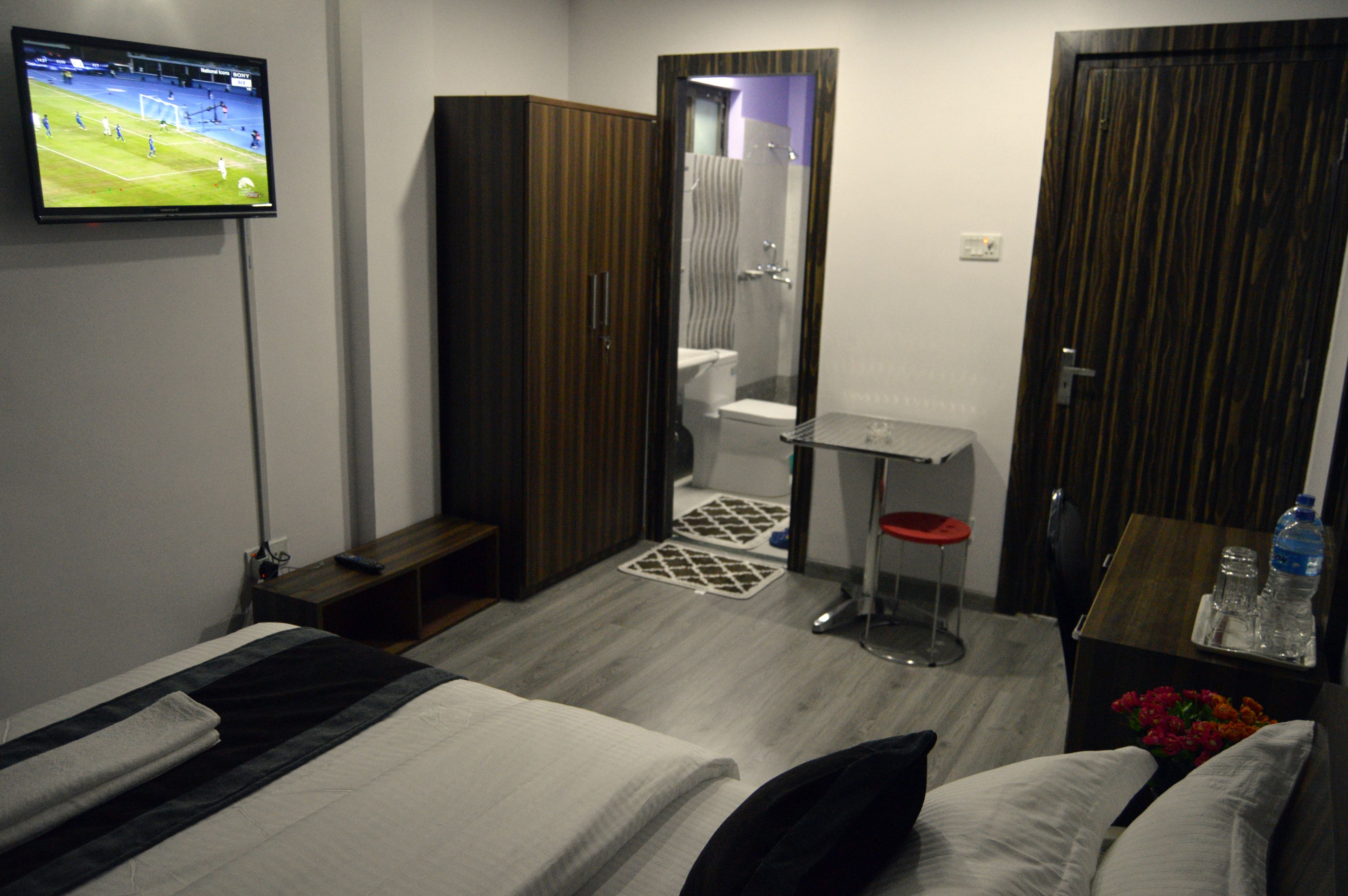 A hotel room with two beds, a TV, a mirror, a shower, and a small table with a water bottle.
