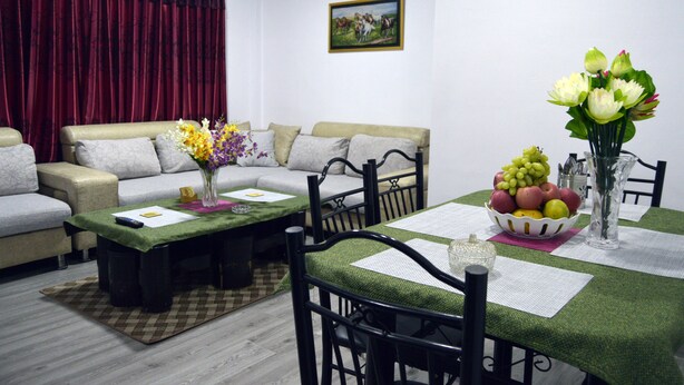 A living room with a sofa, coffee table, and dining table set with a vase of flowers, a bowl of fruit, and a framed picture on the wall. - Nana Homes (Kathmandu)