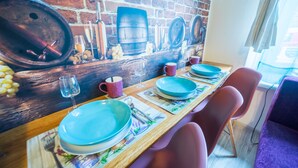 Un espace repas agrémenté d’une fresque murale en briques, d’une table en bois et de chaises violettes.
