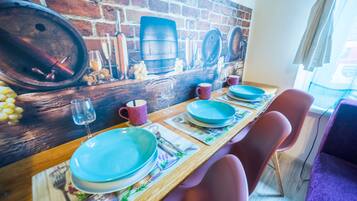 Un comedor con mural de pared de ladrillo, mesa de madera y sillas moradas.