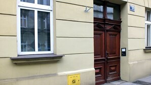 Une façade d’immeuble avec une grande porte en bois, une fenêtre à cadre blanc et une petite enseigne au-dessus de la porte.