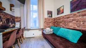 Une pièce chaleureuse avec un mur en briques, un canapé marron agrémenté d’un coussin turquoise, une table à manger avec des chaises et une fenêtre avec des rideaux.