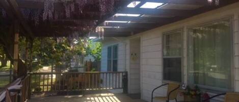 A covered porch with wooden flooring, a table with chairs, and a window overlooking a garden.