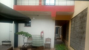 Un patio con baldosas, una mesa, sillas, una planta en maceta y un extintor en la pared.