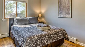 A bedroom with a bed, a nightstand, a lamp, a window, and a painting on the wall. - Elyon Hall CoachHouse, Indiana Dunes Nat’l Park, 10 min hike to Beach (Miller Beach)