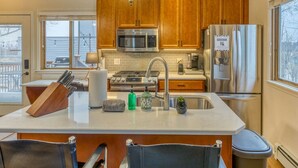 A modern kitchen with wooden cabinets, stainless steel appliances, and a central island with a sink and various items. - Elyon Hall CoachHouse, Indiana Dunes Nat’l Park, 10 min hike to Beach (Miller Beach)