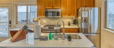 A modern kitchen with wooden cabinets, stainless steel appliances, and a central island with a sink and various items.