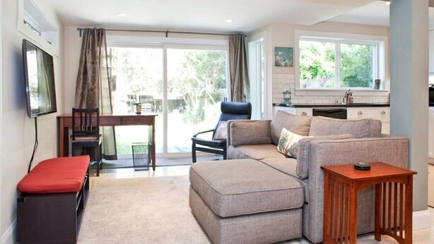 A modern living room with a sofa, a red bench, a wooden table, and a kitchen area with a window. - Charming, modern, private apt in the family-friendly Inner Richmond neighborhood; near GG Park. (San Francisco)