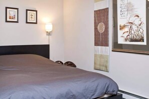 Quarto com cama, duas imagens emolduradas na parede, luminária fixa e um painel decorativo grande.