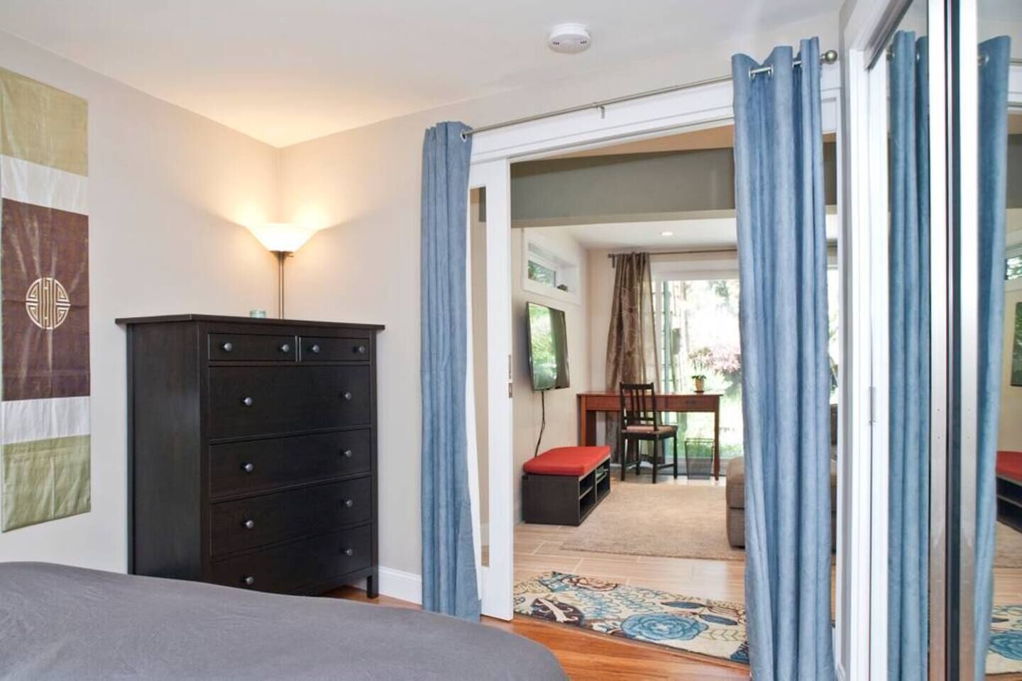Een slaapkamer met een bed, een kaptafel, een bureau met stoel, en uitzicht door een geopende deur.