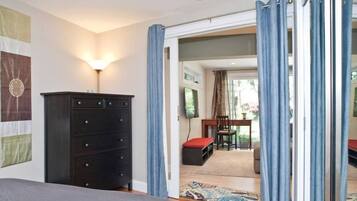 Een slaapkamer met een bed, een kaptafel, een bureau met stoel, en uitzicht door een geopende deur.