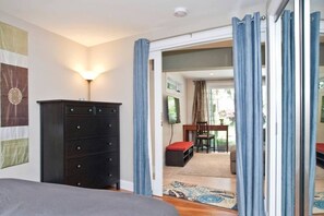 A bedroom with a bed, a dresser, a desk with a chair, and a view through an open door.