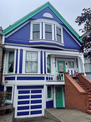 Une maison à deux étages avec une porte d’entrée verte, un garage et un petit porche doté d’un banc.