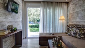 A modern living room with a sofa, a coffee table with decorative items, a TV mounted on the wall, and a large window with curtains. - Luxury Villa Fotini (Thasos)