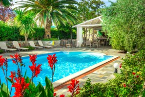 A swimming pool with lounge chairs, a pergola, and lush greenery. - Luxury Villa Fotini (Thasos)