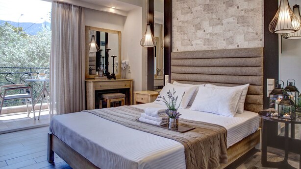 A modern bedroom with a large bed, a desk, and a balcony with a table and chairs. - Luxury Villa Fotini (Thasos)