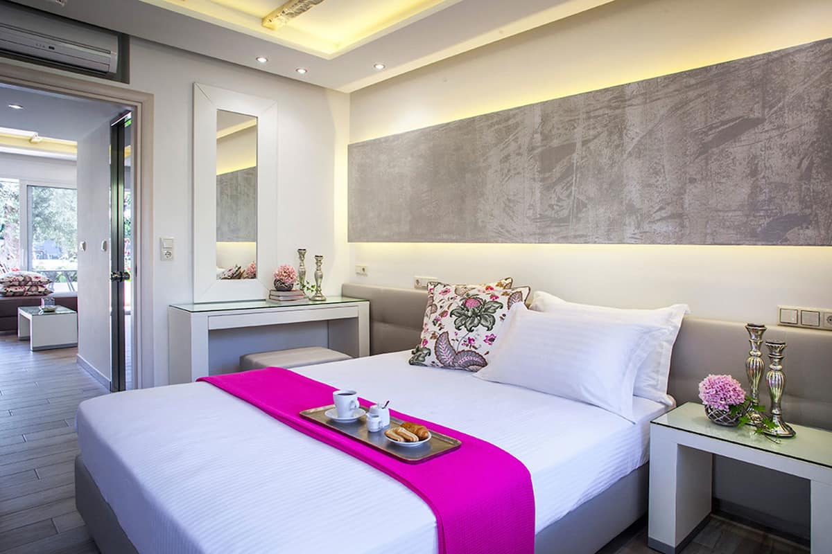 A modern hotel room with a large bed, a glass desk, and a view of the outdoors.