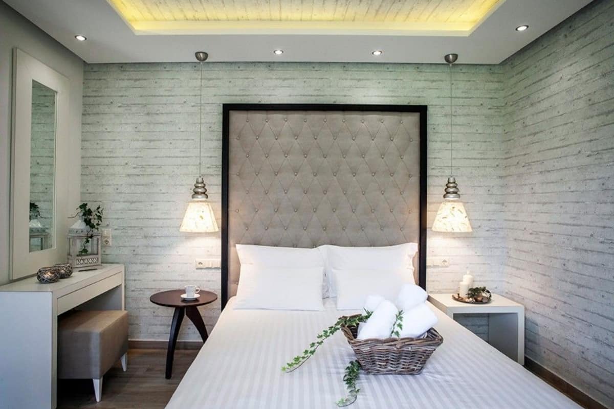 A modern bedroom with a tufted headboard, a bedside table with a lamp, a small round table, and a basket of towels.