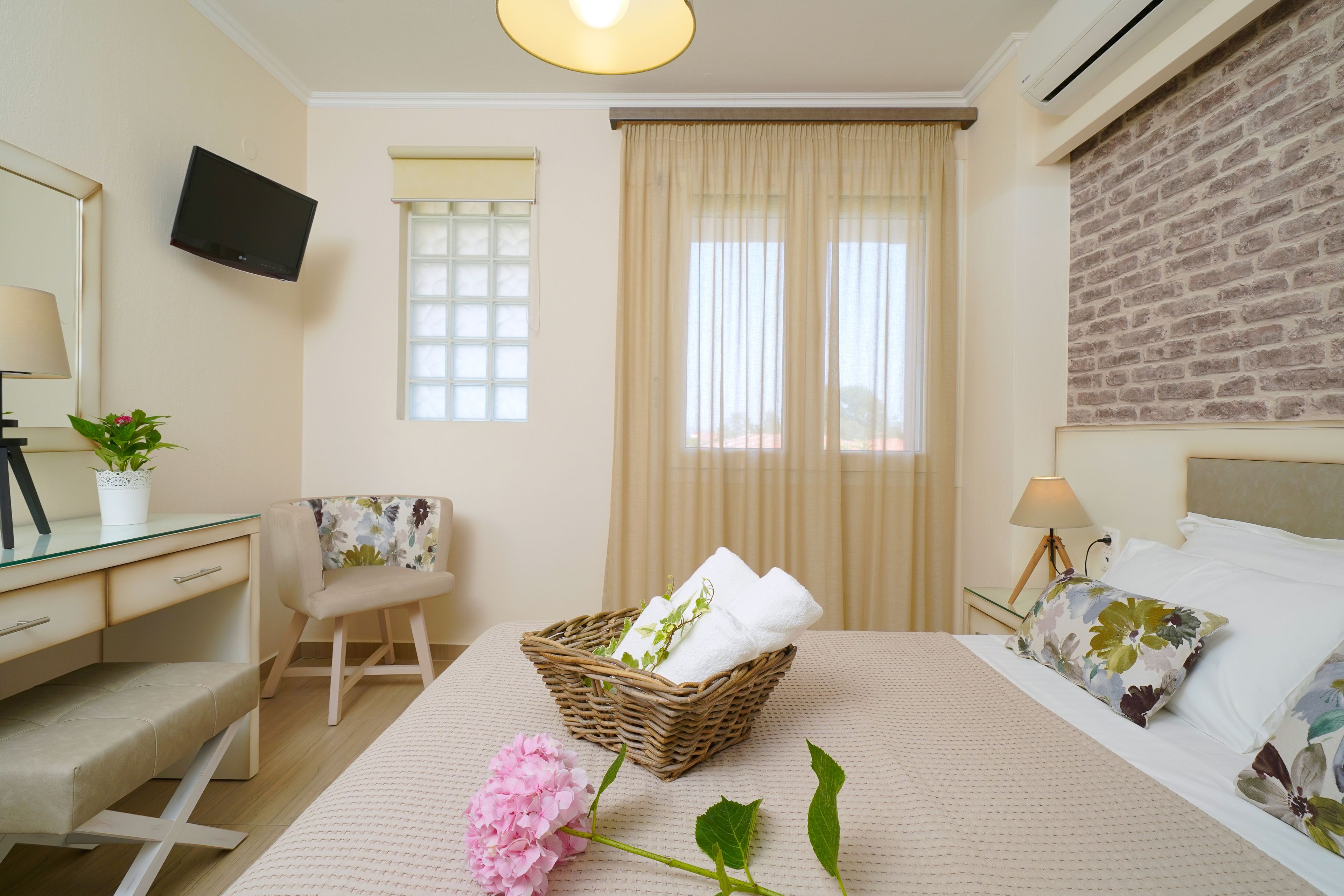 A hotel room with a bed, a desk, a chair, a TV mounted on the wall, and a window with curtains.
